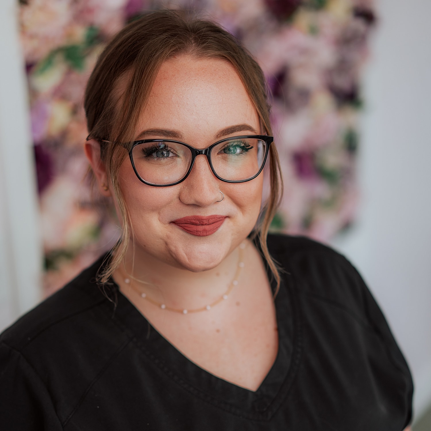 Smiling woman in black scrubs with glasses.