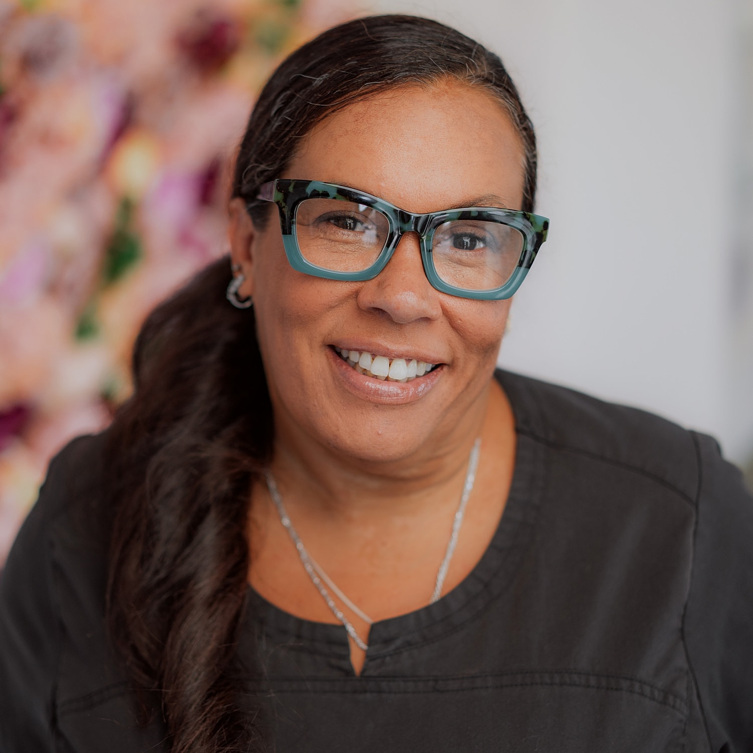 Woman smiling with glasses against floral background.