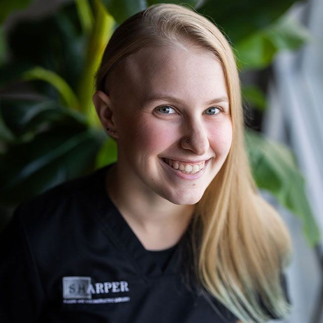 Smiling person with long hair and plant backdrop.