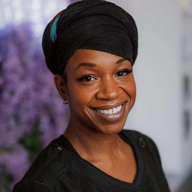 Smiling woman with headwrap and floral background.