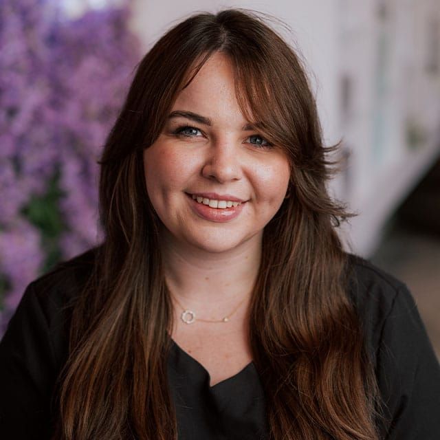 Woman smiling in front of purple flowers.