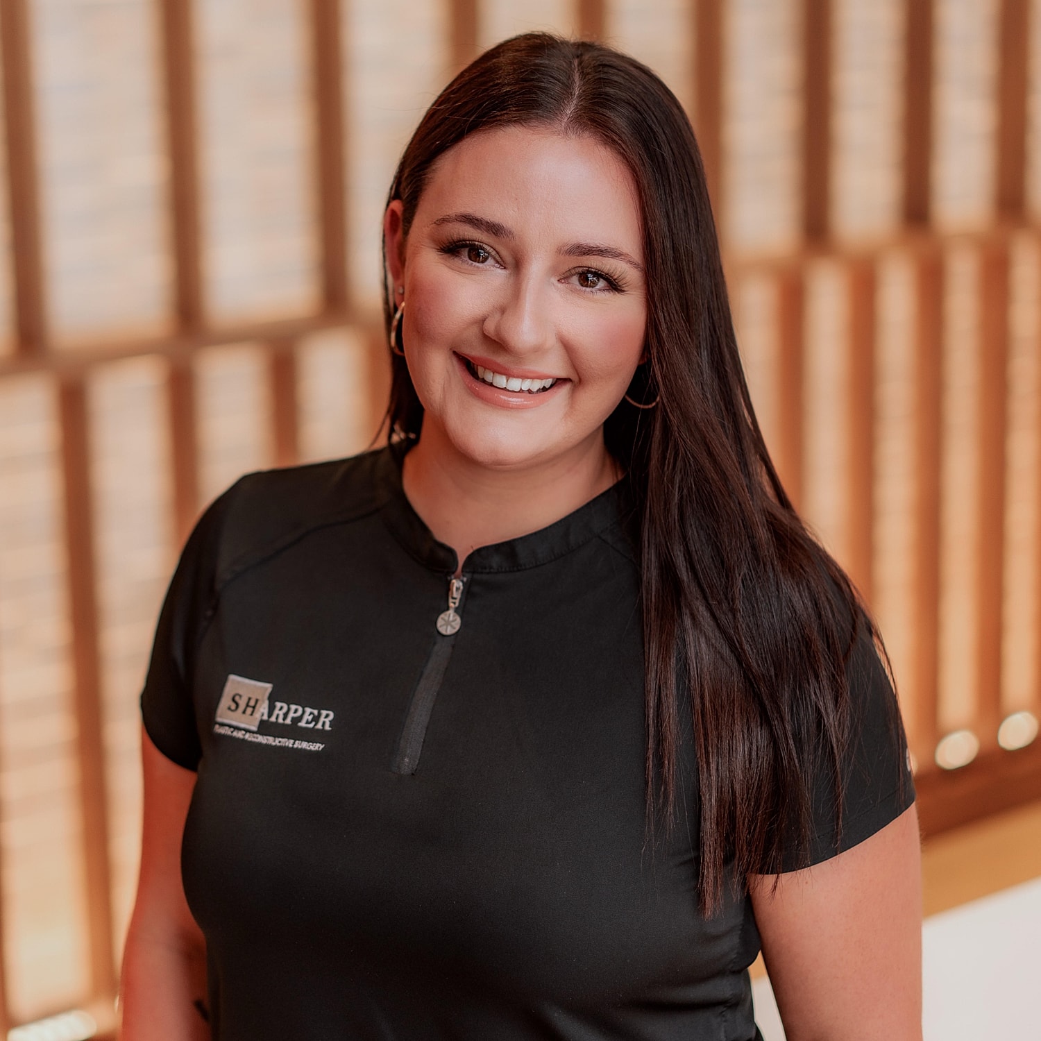 Smiling woman in surgical attire, promoting surgery.