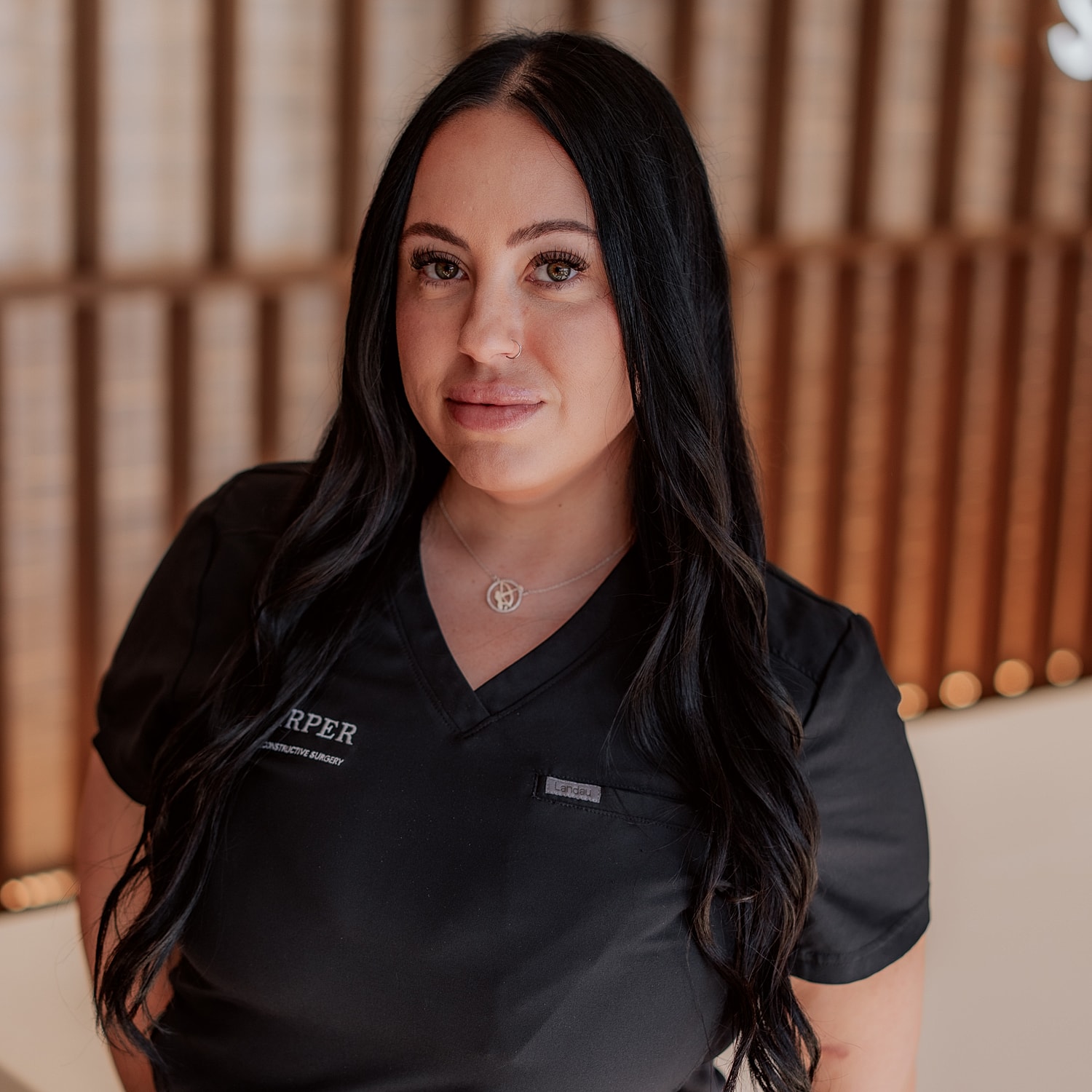Smiling woman in scrubs with floral background.