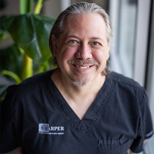 Smiling person in medical scrubs with plant.