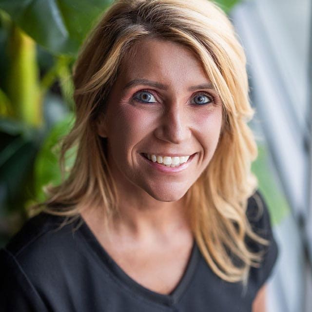 Smiling woman with blonde hair against greenery.