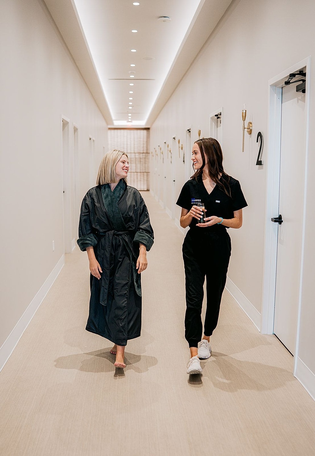 Two women walking down a spa hallway.