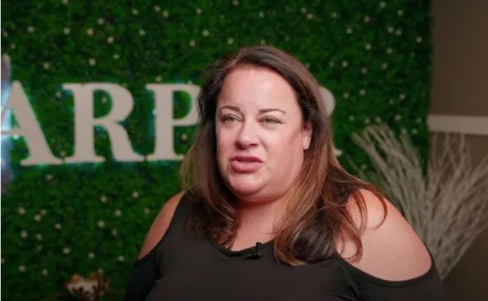 Person speaking in front of green backdrop.