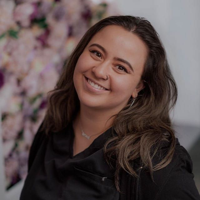 Smiling person with wavy hair against floral background.
