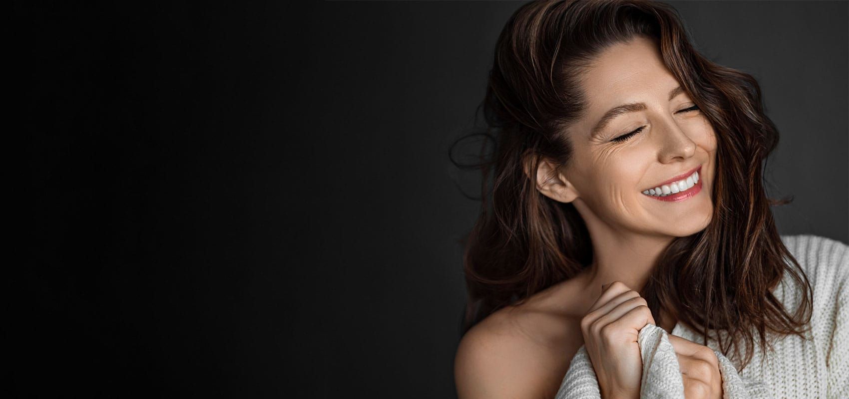 Smiling woman in cozy sweater against dark background.