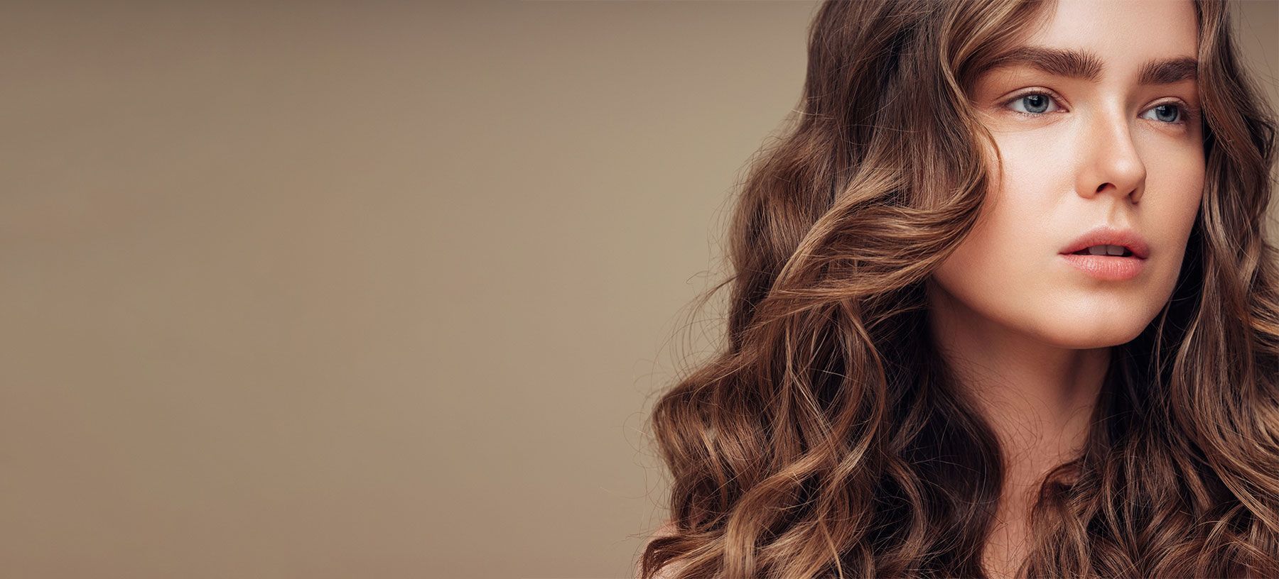 Young woman with wavy hair against neutral background.