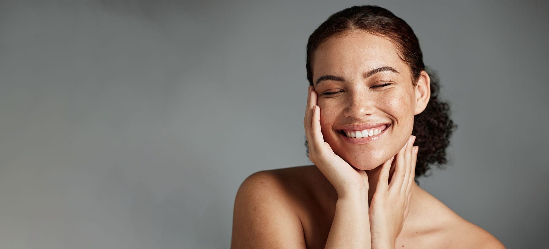 Smiling woman with curly hair, touching her face.